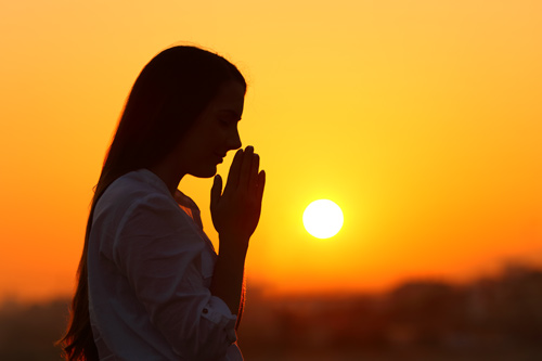 woman praying with sunset in background