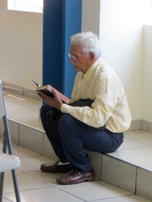 Man in El Salvador sitting and reading Bible with new eyeglasses.