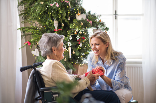 woman visiting and giving Christmas present to a senior woman in wheelchair