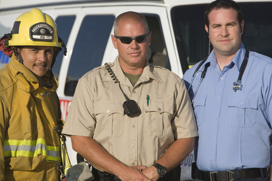 firefighter, police officer, EMT standing next to each other in front of emergency vehicle